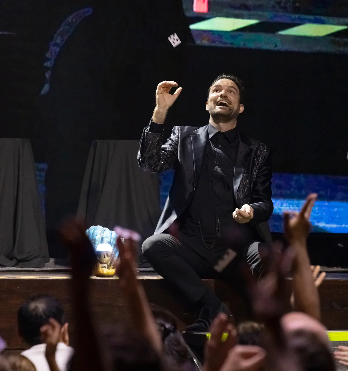 Fernando Mier throws a card into the air in front of an audience with raised hands.