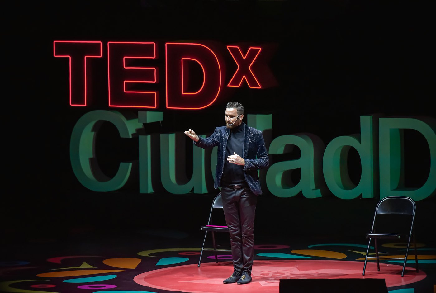 Fernando Mier en el escenario de una charla TEDx, junto a dos sillas vacías